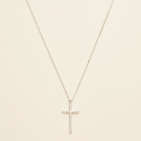 Silver dainty cross necklace on warm cream background